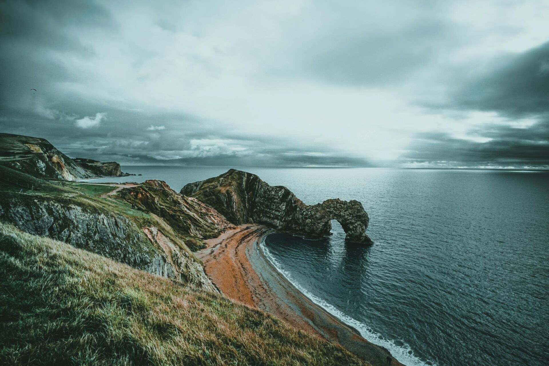 Scenic view of Durdle Door arch along the Jurassic Coastline in England under dramatic skies.