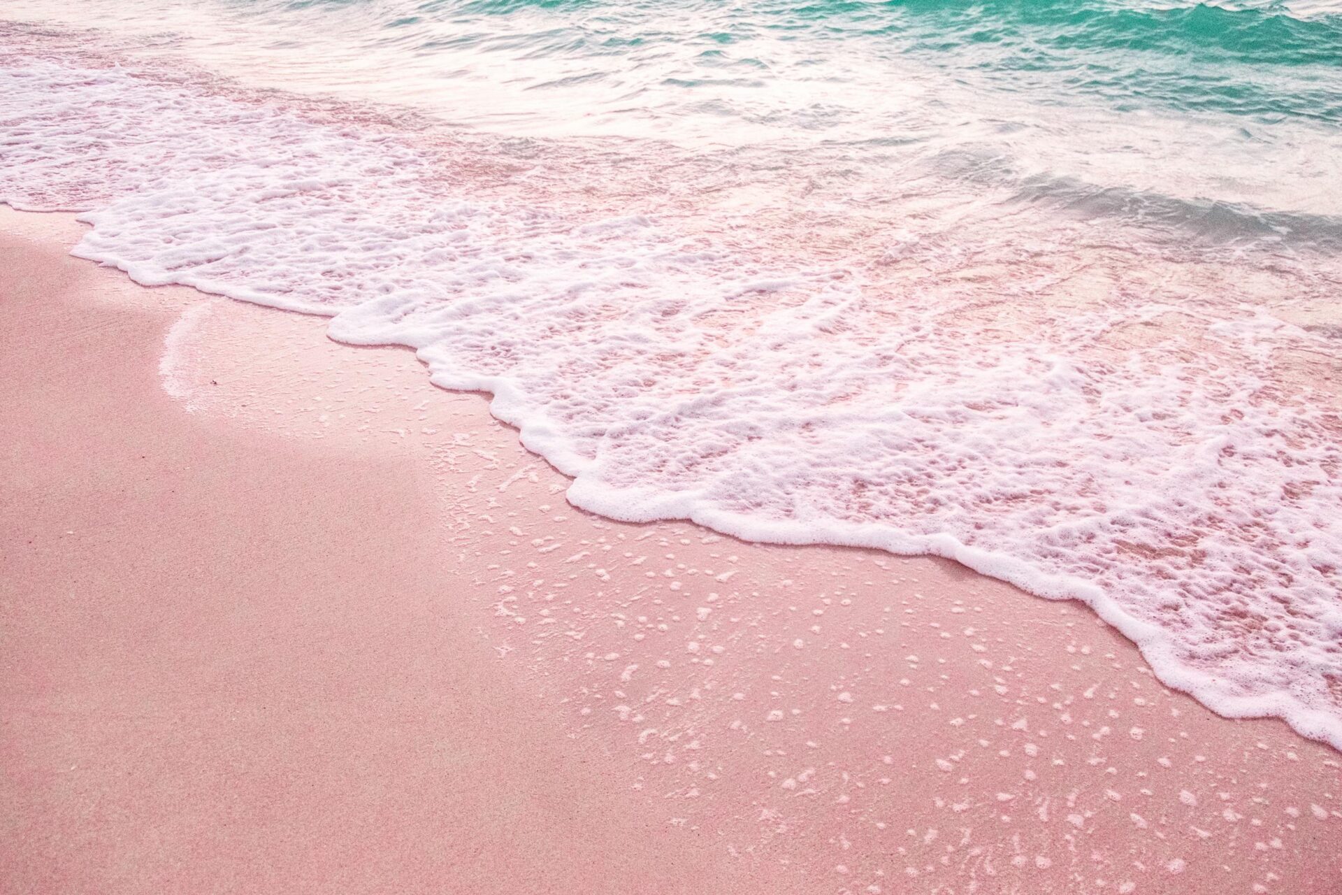 A tranquil scene of a pink sandy beach with gentle waves lapping at the shore under daylight.