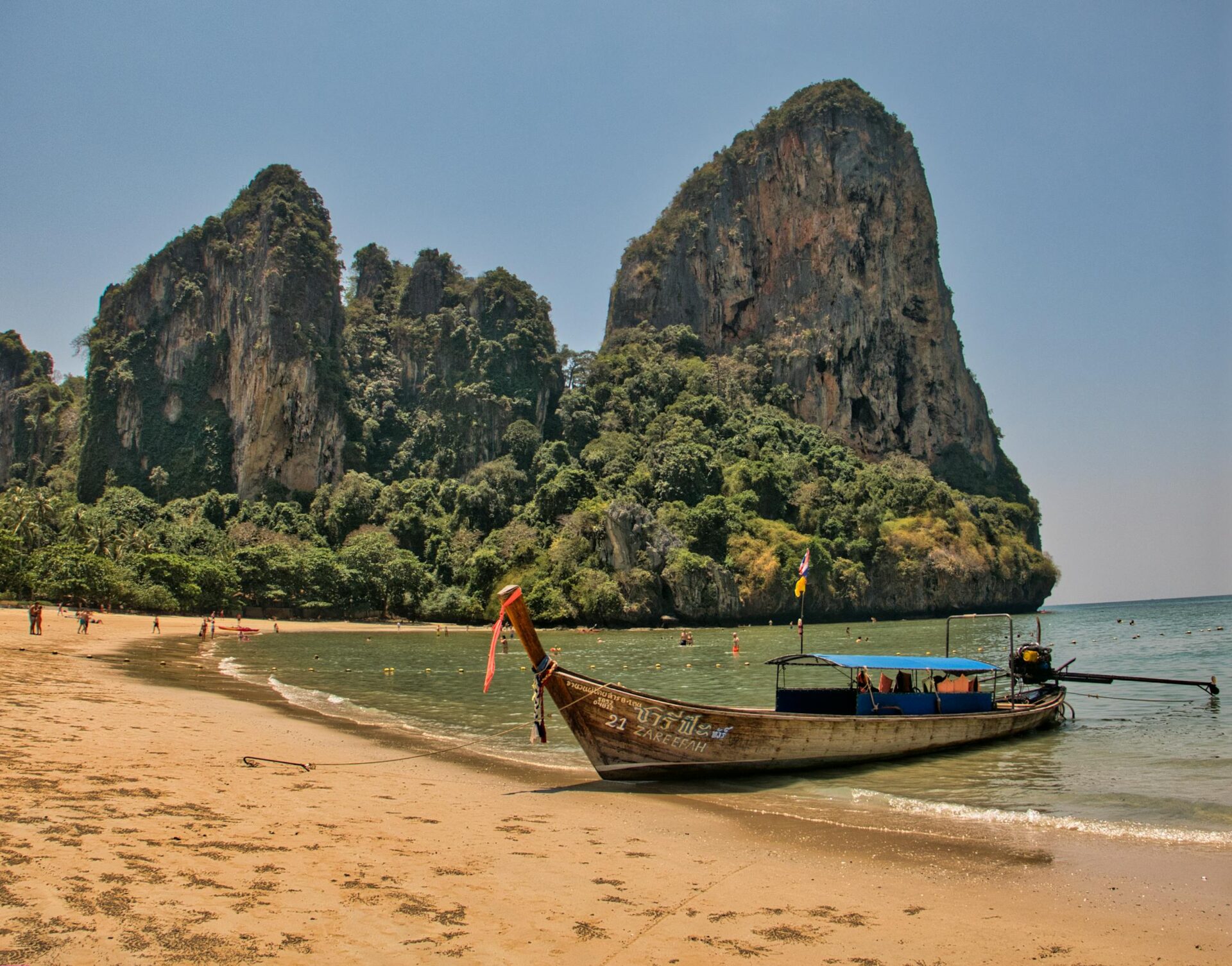 Longtail boat docked on the sandy shore of Railay Beach with stunning limestone cliffs in the background.